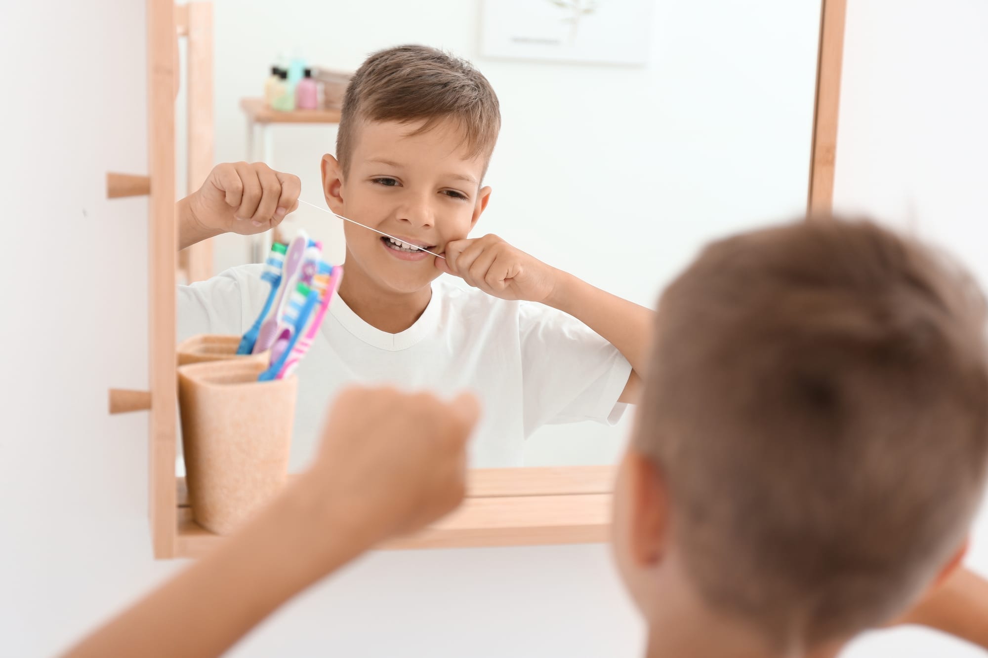 Little boy flossing teeth in bathroom mirror
