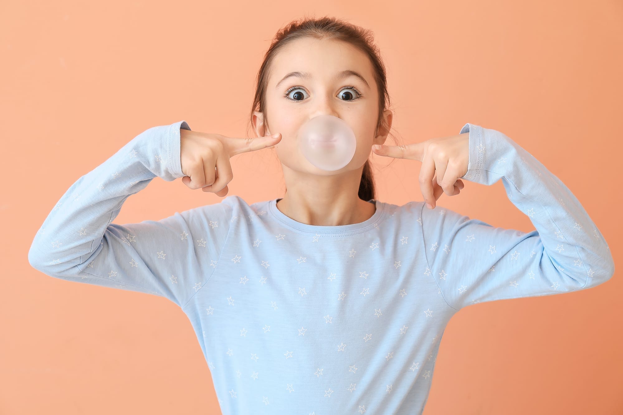 little girl blowing bubble with gum on peach background