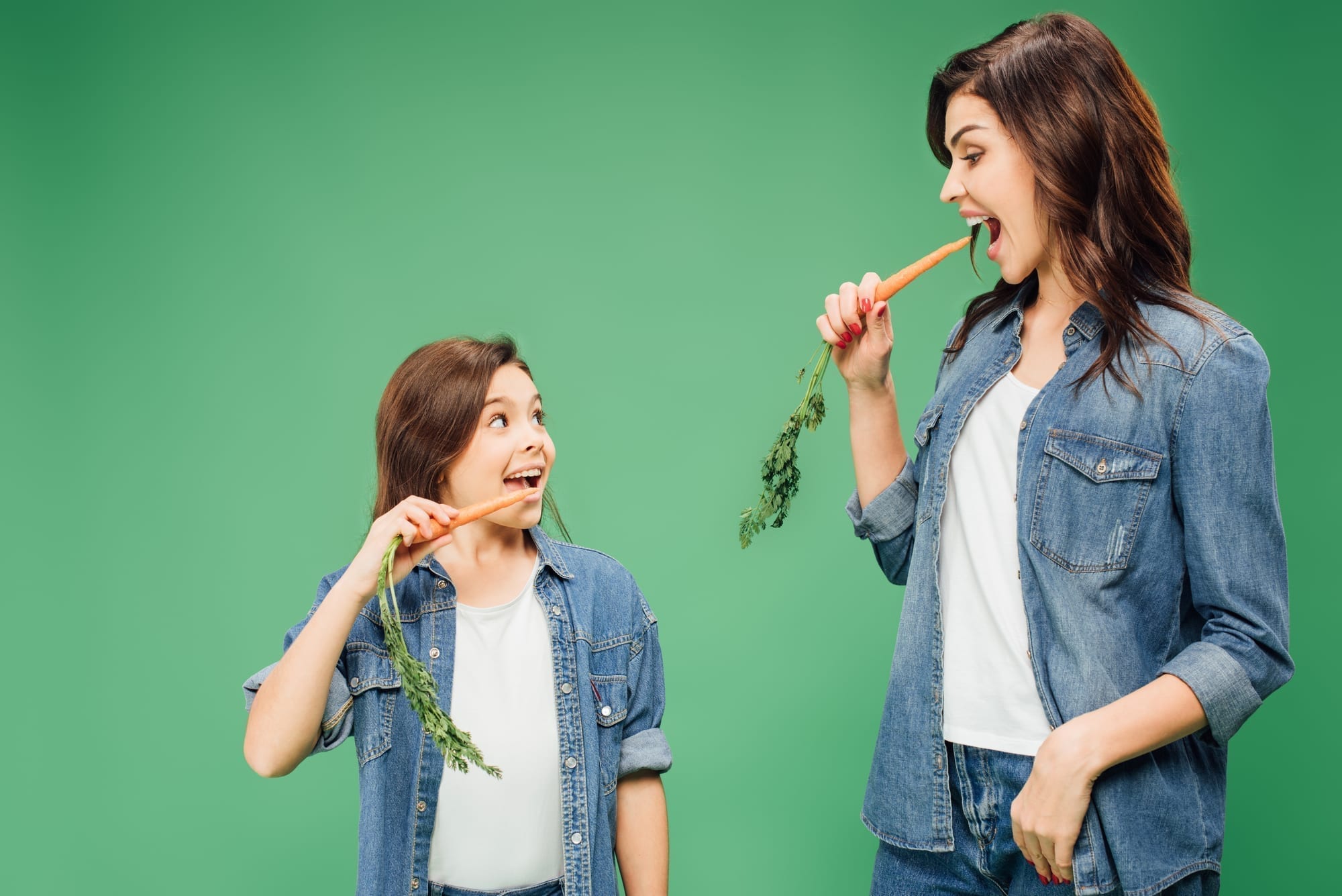 mom and daughter eating carrots on green background