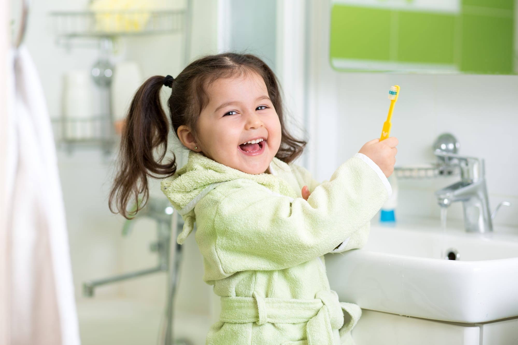 happy little girl brushing her teeth in bathroom