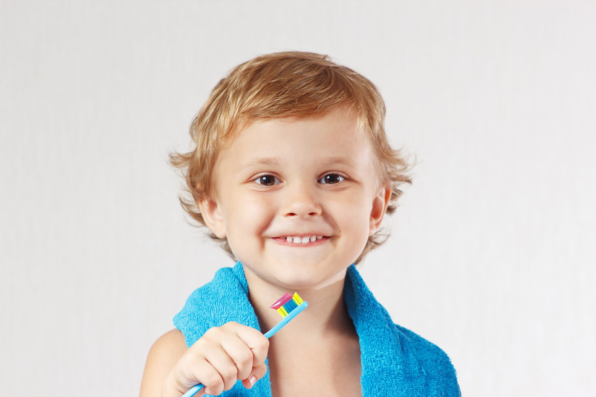 Young cute blond boy with toothbrush with pink toothpaste on a white background