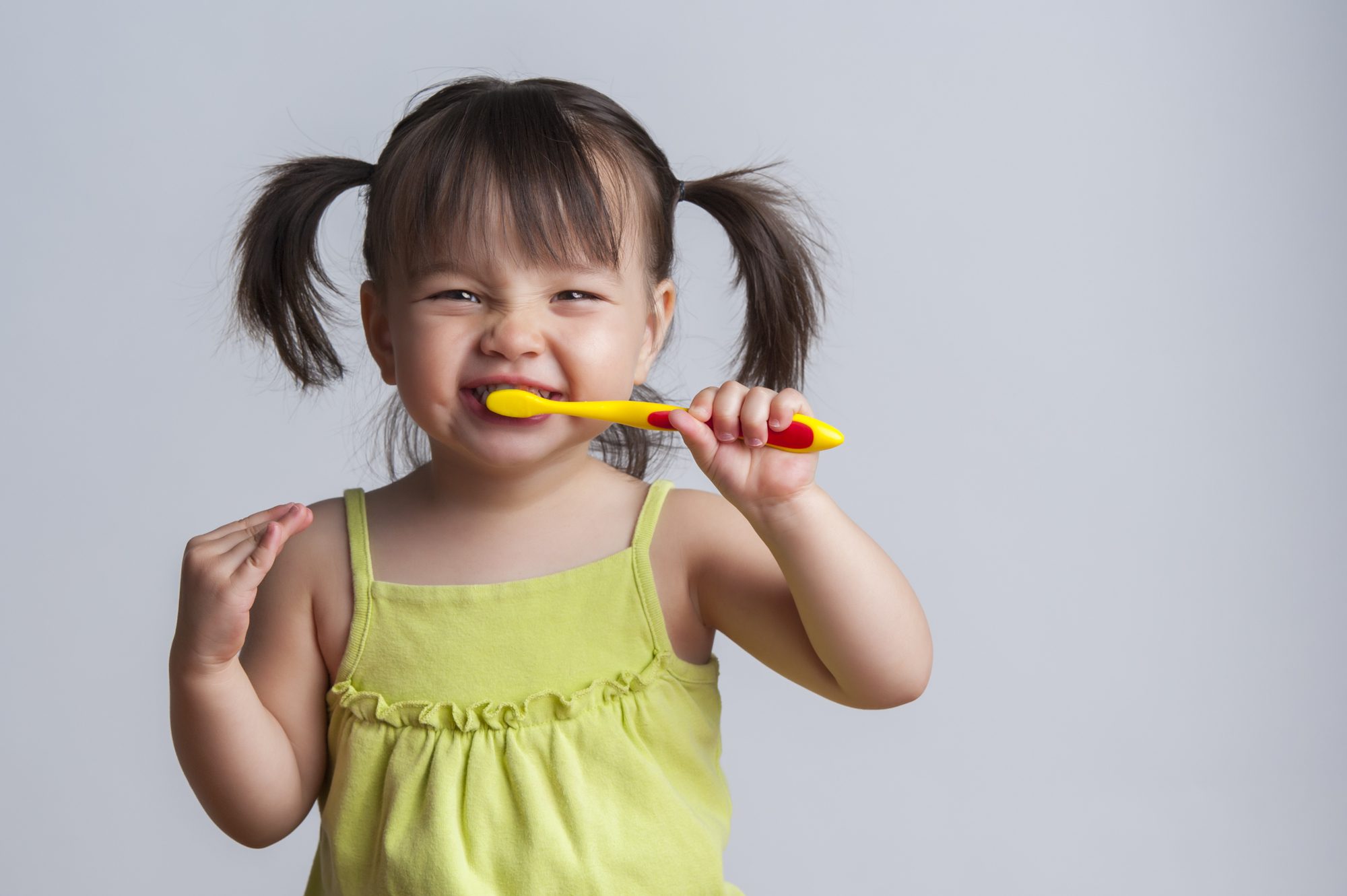 Toddler smiling while brushing her teeth as part of her daily dental hygiene routine