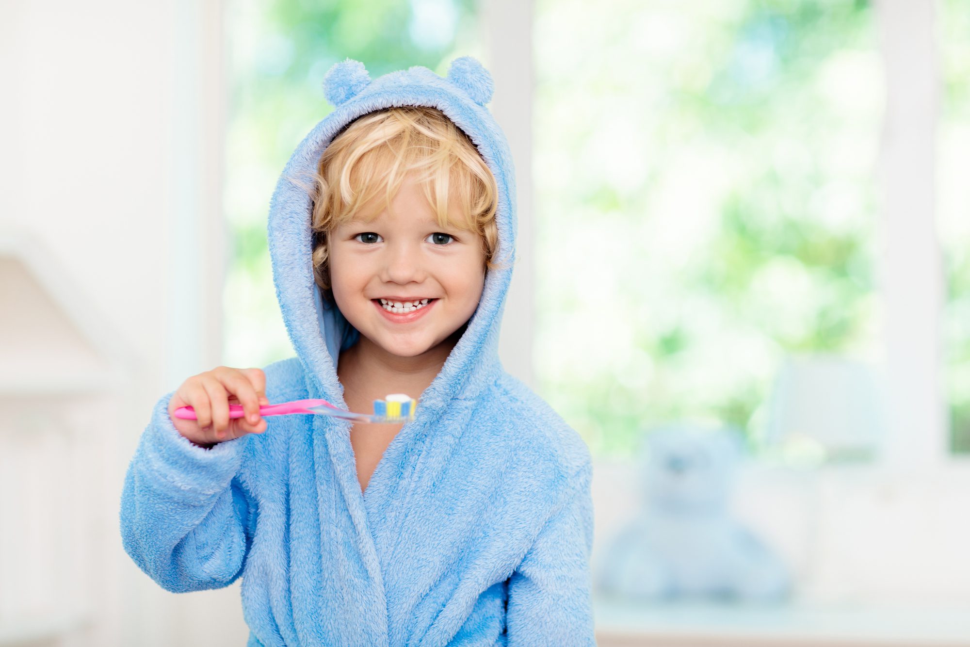 Young boy in blue robe brushing teeth with toothpaste with fluoride