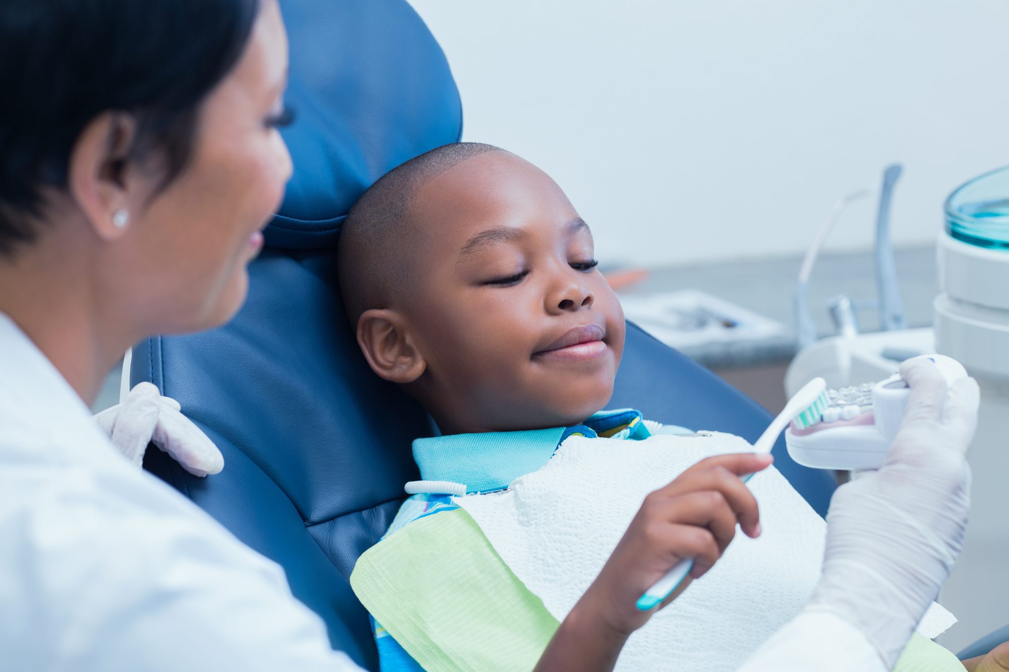 Female dental hygienist showing young boy how to clean teeth