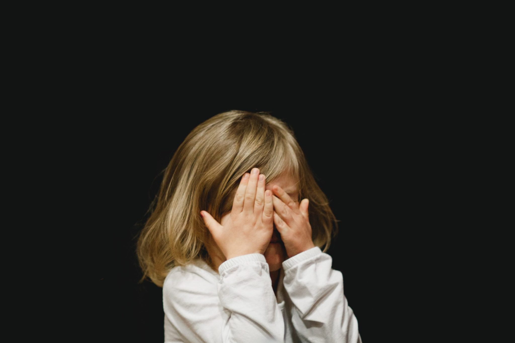 little girl covering her face on black background