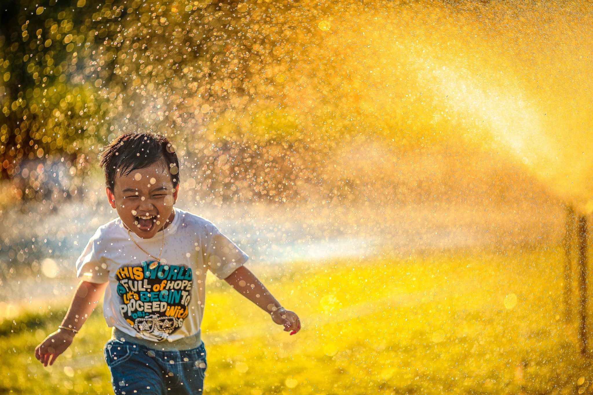 Happy little boy running through a sprinkler
